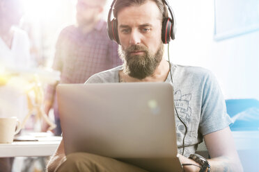 Seriöser männlicher Design-Profi mit Kopfhörern und Laptop im Büro - CAIF09261