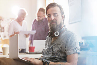 Porträt lächelnd männlich Design-Profi mit Kopfhörer mit Laptop im Büro - CAIF09265