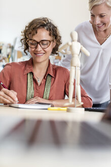Weibliche Design-Profis mit Künstlerfigur beim Skizzieren im Büro - CAIF09270