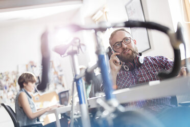 Fahrrad lehnt gegen Schreibtisch neben männlichen Design-Profi sprechen auf Handy im Büro - CAIF09283