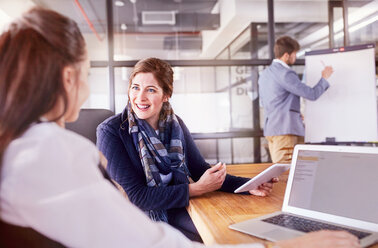 Smiling businesswomen with digital tablet and laptop talking in conference room meeting - CAIF09292