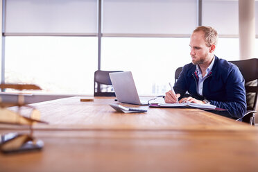 Konzentrierter Geschäftsmann macht sich Notizen am Laptop im Konferenzraum - CAIF09297