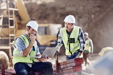 Foreman and construction worker using laptop at construction site - CAIF09306