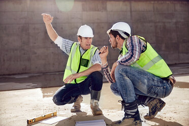 Bauarbeiter und Ingenieur unterhalten sich auf einer sonnigen Baustelle - CAIF09309