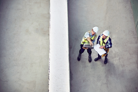 Bauarbeiter und Ingenieur mit Laptop im Gespräch auf der Baustelle, lizenzfreies Stockfoto