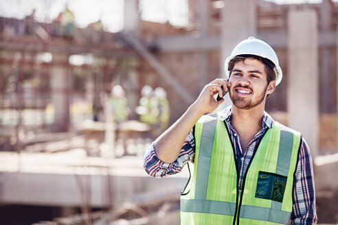 Bauarbeiter, der auf einer sonnigen Baustelle mit seinem Handy telefoniert - CAIF09318