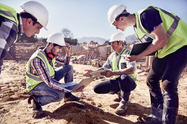 Construction workers and engineers using digital tablets at sunny construction site - CAIF09321