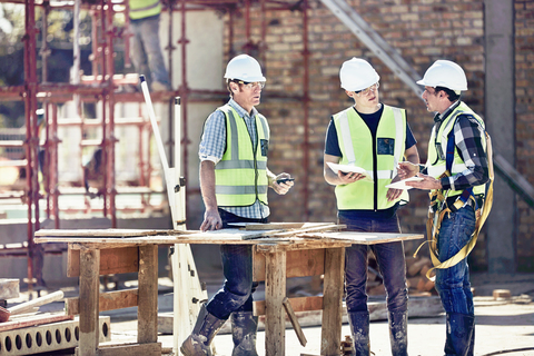 Bauarbeiter und Polier im Gespräch auf einer sonnigen Baustelle, lizenzfreies Stockfoto