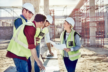 Vorarbeiterin im Gespräch mit Bauarbeitern auf einer sonnigen Baustelle - CAIF09325