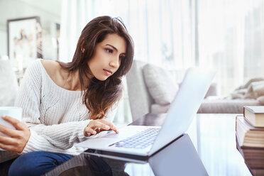 Serious woman using laptop at dining table - CAIF09327