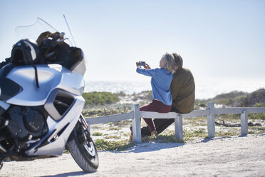 Älteres Paar nimmt Selfie am sonnigen Straßenrand in der Nähe von Motorrad - CAIF09333