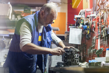 Älterer männlicher Motorradmechaniker, der ein Motorteil in der Werkstatt repariert - CAIF09342