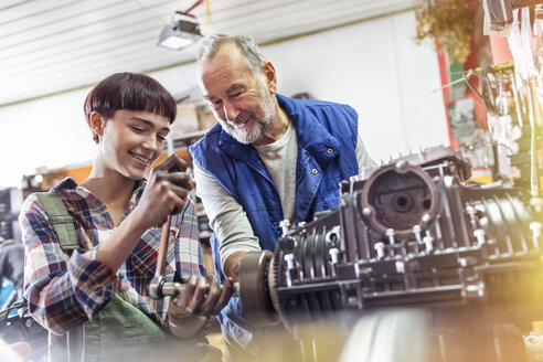 Männliche und weibliche Motorradmechaniker reparieren einen Motor in einer Werkstatt - CAIF09347