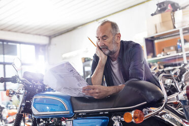 Fokussierter älterer männlicher Motorradmechaniker bei der Überprüfung des Handbuchs in der Werkstatt - CAIF09355