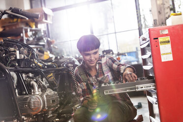 Motorradmechanikerin holt Werkzeug aus dem Werkzeugkasten in der Werkstatt - CAIF09361