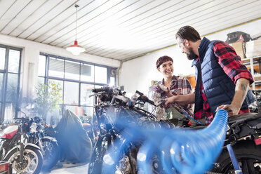 Männliche und weibliche Motorradmechaniker reparieren ein Motorrad in einer Werkstatt - CAIF09366