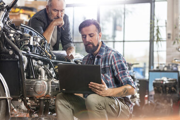 Männlicher Motorradmechaniker mit Laptop in der Werkstatt - CAIF09370