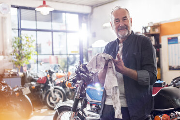 Porträt lächelnder älterer männlicher Motorradmechaniker, der sich in einer Werkstatt die Hände am Lappen abwischt - CAIF09371