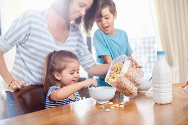 Mother pouring cereal for daughter at breakfast table - CAIF09378