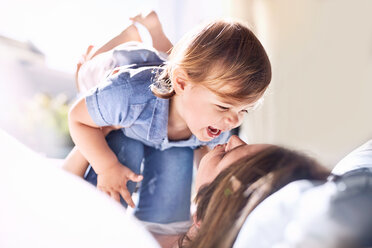 Playful mother holding laughing baby son on knees - CAIF09381