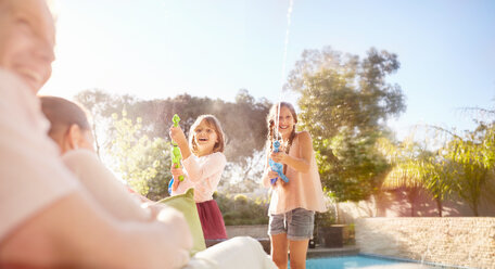 Verspielte Schwestern mit Spritzpistolen, die im sonnigen Sommer am Pool Wasser versprühen - CAIF09382