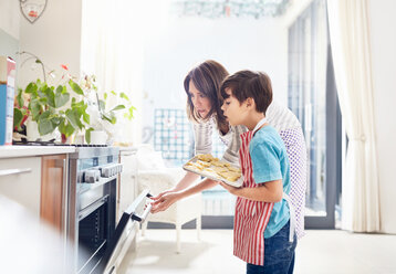 Mutter und Sohn backen und schieben Kekse in den Ofen in der Küche - CAIF09386
