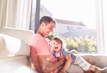 Affectionate father holding baby son in sunny living room - CAIF09389