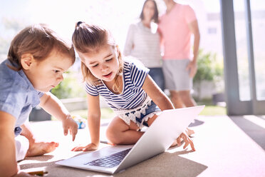 Bruder und Schwester benutzen Laptop auf sonnigem Boden - CAIF09391