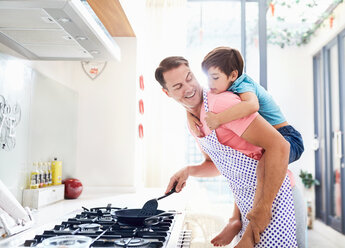 Father piggybacking son, cooking at stove in kitchen - CAIF09392