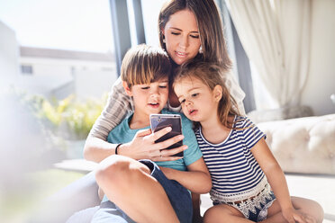 Mutter und Kinder benutzen ein Handy im sonnigen Wohnzimmer - CAIF09396