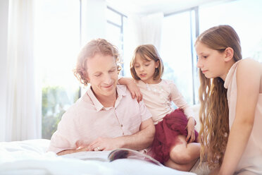 Vater und Töchter lesen ein Buch auf dem Bett - CAIF09402