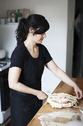 Frau bereitet Rhabarberkuchen vor, während sie an der Küchentheke steht - CAVF04443