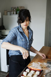 Woman sprinkling flour on cookies - CAVF04457