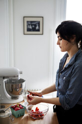 Frau schneidet Erdbeeren, während sie in der Küche zu Hause steht - CAVF04459