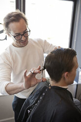 Friseur schneidet einem Mann die Haare mit einer Schere im Friseursalon - CAVF04491