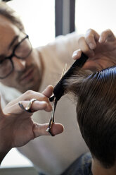 Barber cutting young man's hair in salon - CAVF04494