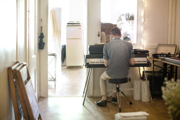 Rear view of man playing piano at home - CAVF04502