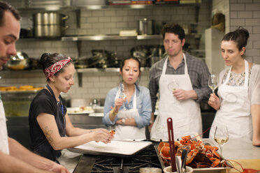 Students looking at female chef preparing food at commercial kitchen - CAVF04525