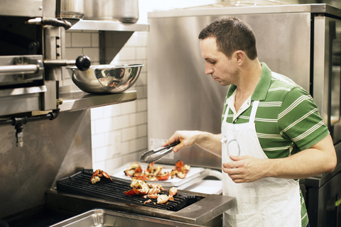 Mann bereitet Essen am Grill in einer Großküche zu, lizenzfreies Stockfoto