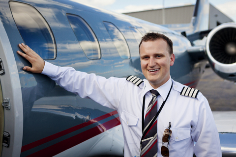 Porträt eines glücklichen Piloten, der neben einem Flugzeug steht, lizenzfreies Stockfoto