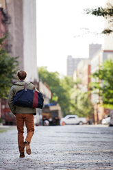 Rückansicht eines Mannes, der eine Tasche trägt, während er auf der Straße geht - CAVF04587