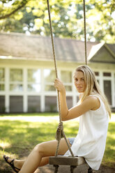 Portrait of woman sitting on swing against house - CAVF04618
