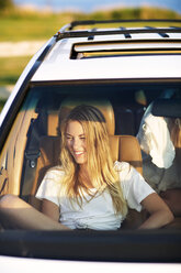 Lächelnde Frau, die wegschaut, während sie im Auto sitzt - CAVF04643