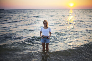 Porträt einer Frau mit Händen in den Taschen im Wasser stehend am Strand - CAVF04650