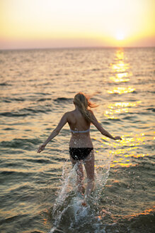 Rückansicht einer Frau, die bei Sonnenuntergang am Strand läuft - CAVF04651