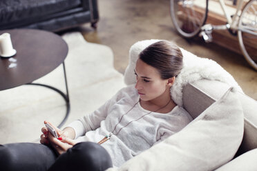 Hochformatige Ansicht einer Frau, die ein Mobiltelefon benutzt, während sie zu Hause auf dem Sofa liegt - CAVF04674