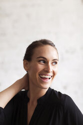 Cheerful woman looking away while standing against wall - CAVF04682