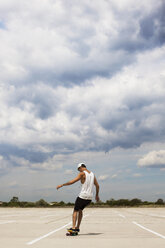 Rear view of man skateboarding on field against cloudy sky - CAVF04698