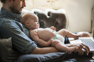 Ausgeschnittenes Bild eines Mannes, der einen Laptop benutzt, während er mit seinem Sohn zu Hause sitzt - CAVF04712