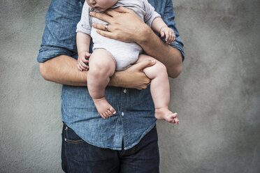 Mittelteil eines Mannes, der ein Baby trägt, während er an der Wand steht - CAVF04720